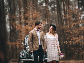 Romantic fairytale wedding couple, bride and groom, kissing and embracing in pine forest near retro car.
