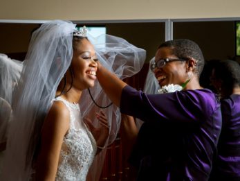 Mother of the bride adjusts her daughter’s veil on her wedding day.  Beautiful, African American women, smiling while getting the daughter ready for her wedding.